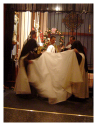 Mother Prioress and the Novice Mistress help clothe the Novice in the choir mantle Mother Prioress and the Novice Mistress help clothe the Novice in the choir mantle