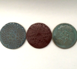 Coasters with various designs shown in quinn's blue, burgundy and turquoise glazes.