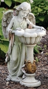 Solar angel birdbath garden statue standing on mulch in front of shrub.