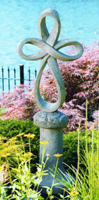 Eternity cross standing on pedestal in a garden bed by water. 
