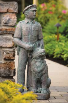 Law enforcement officer with dog statue on stone path.