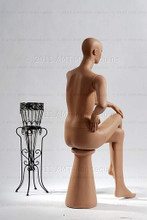 In this full body rear view, naked mannequin Emily sits with her right leg crossed over her left and her left hand resting on her right knee. Her right hand is at her waist.   With pierced ears, mannequin Emily can display earrings and jewelry.  Pedestal included.