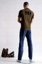 In this full body rear view photo, wearing a casual olive-green t-shirt and jeans with shoes,  mannequin Bill, stands with his legs even, his arms raised to his waist with his left hand almost touching his right arm.  Mannequin Bill can be displayed with or without a wig / hairpiece.  Glass stand and support hardware included.