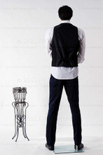 In this full body rear view photo, wearing a black pants, a white shirt, black vest,  shoes and a short dark brunette wig / hairpiece,  mannequin Bill, stands with his legs even, his arms raised to his waist with his left hand almost touching his right arm.  Mannequin Bill can be displayed with or without a wig / hairpiece.  Glass stand and support hardware included.