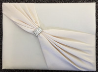 Ivory Satin Sash Guest Book.
This elegant ivory satin guest book is decorated on the front with an ivory satin sash and rhinestone ornament. The book measures 8.5" x 6" and holds 55 pages for a total of 990 signatures.