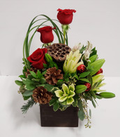 A cheerful holiday centerpiece with red roses, white lilies, pinecones, and other Christmas ornament pieces to brighten your days 