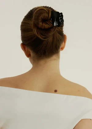Lifestyle view of a person with a hair bun wearing the black scalloped Muse clip against a light wall