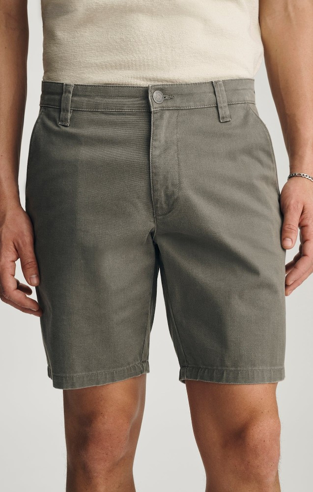 Close-up detail view of the olive vintage colored stretch denim texture, front button, and pocket detail