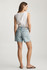 Full-length  back view portrait of model wearing bleached linen denim Mavi Nella high rise relaxed shorts styled casually