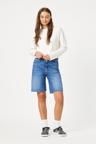 Full-length portrait of model wearing mid brushed classic blue Mavi Heidi high rise cuffed shorts styled casually