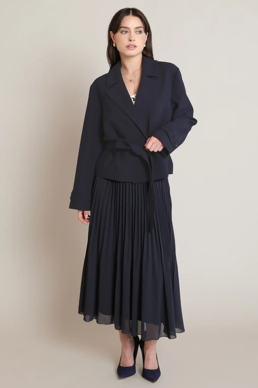 Full-length portrait of model wearing Black Tape navy pleated midi skirt styled with boots