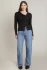 Full-length portrait of model wearing Black Tape asymmetric button top styled with tailored trousers