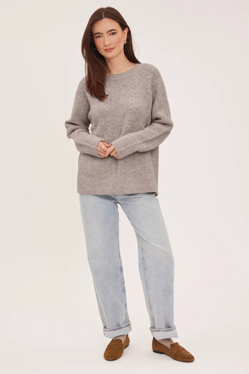 Full-length portrait of model wearing heather pebble grey Gentle Fawn Lori cable knit sweater styled with denim