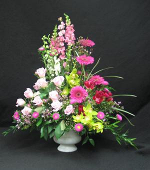A beautiful pink and green arrangement featuring green cymbidium orchids, pink roses and larkspur or snapdragons.