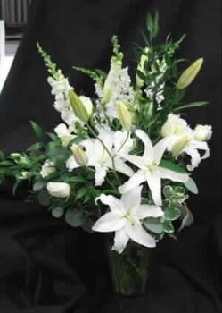 Our Churchill arrangement is a lovely vase of Oriental Lilies in white, Snapdragons, white Escimo roses , white Alstroemeria, mixed foliage.Hatcher original. Styled in a glass vase. Send to the funeral home, or residence