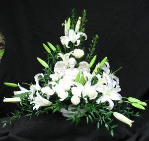 An Angel figurine nestled amongst a stunning white combination of white Escimo roses, Siberia oriental lilies, and mixed foliages. We deliver to Kane, Jerrett, Simple Alternative, Newbigging, Trull, and Humprey Funeral homes. We also service all the other homes in Toronto, and the GTA. Hatcher original design.