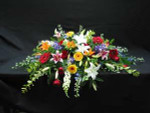 A casket spray for an open casket. Blue Delphinium, red and yellow Gerbera, white Siberia Lilies, pink Star Fighter Lilies, white Snapdragons, mixed foliage, orange Asiatic Lilies, and vibrant red Roses.