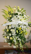A large white and yellow standing spray made by Hatcher Florist. Snapdragons, orchids, gerbera, carnations and large white Oriental Siberia lilies.