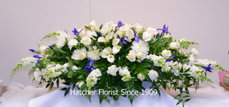 A blue and white flower casket spray. A peaceful combination of lilies, roses, snapdragons, and blue iris.