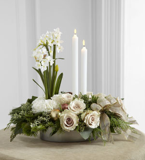 The FTD® Glowing Elegance™ Centerpiece is a departure from the everyday arrangement, stepping into a design blooming with modern sophistication. Exquisite white roses and standard carnations are brought together with assorted holiday greens and seeded eucalyptus at the base of the arrangement accented by copper glass balls and a gold glitter ribbon. Blooming from the base is a spray of white narcissus stems standing next to 2 white taper candles for an eye-catching look that will lend itself to making your holiday festivities both merry and bright. 