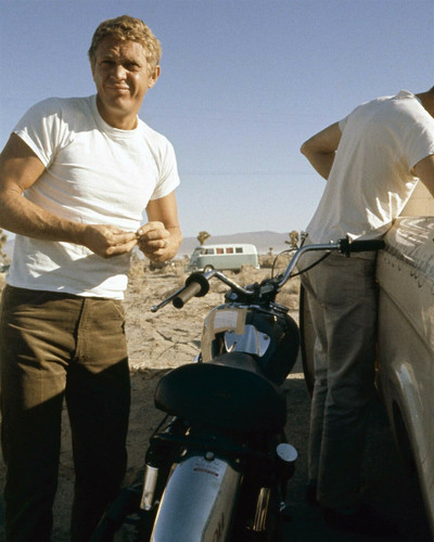 Steve McQueen in white t-shirt stands next to bike in desert 1960's ...