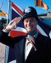 Larry Hagman smiling as he salutes wearing British police helmet 8x10 photo