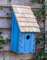 Brand new bird bunkhouse featuring a steep pitched roof. Crafted of wood and accented with a cypress-shingled roof. front opening for easy cleaning.  hand painted in a blue hue with light distressing.