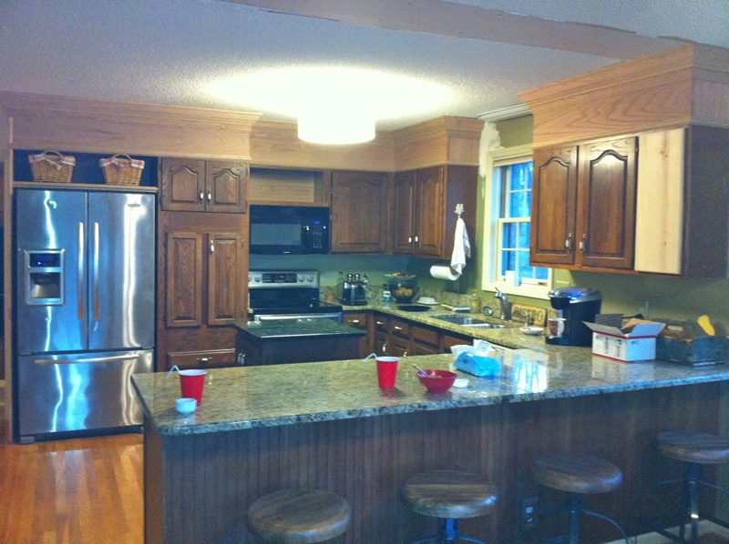 Before shot of a kitchen with dark oak cabinets and popcorn ceiling.